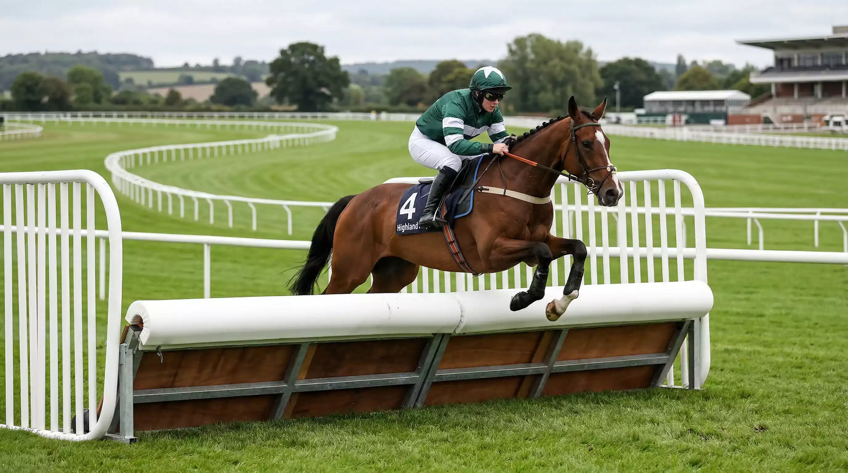 A horse and jockey clearing a padded hurdle on a British racecourse during a National Hunt race